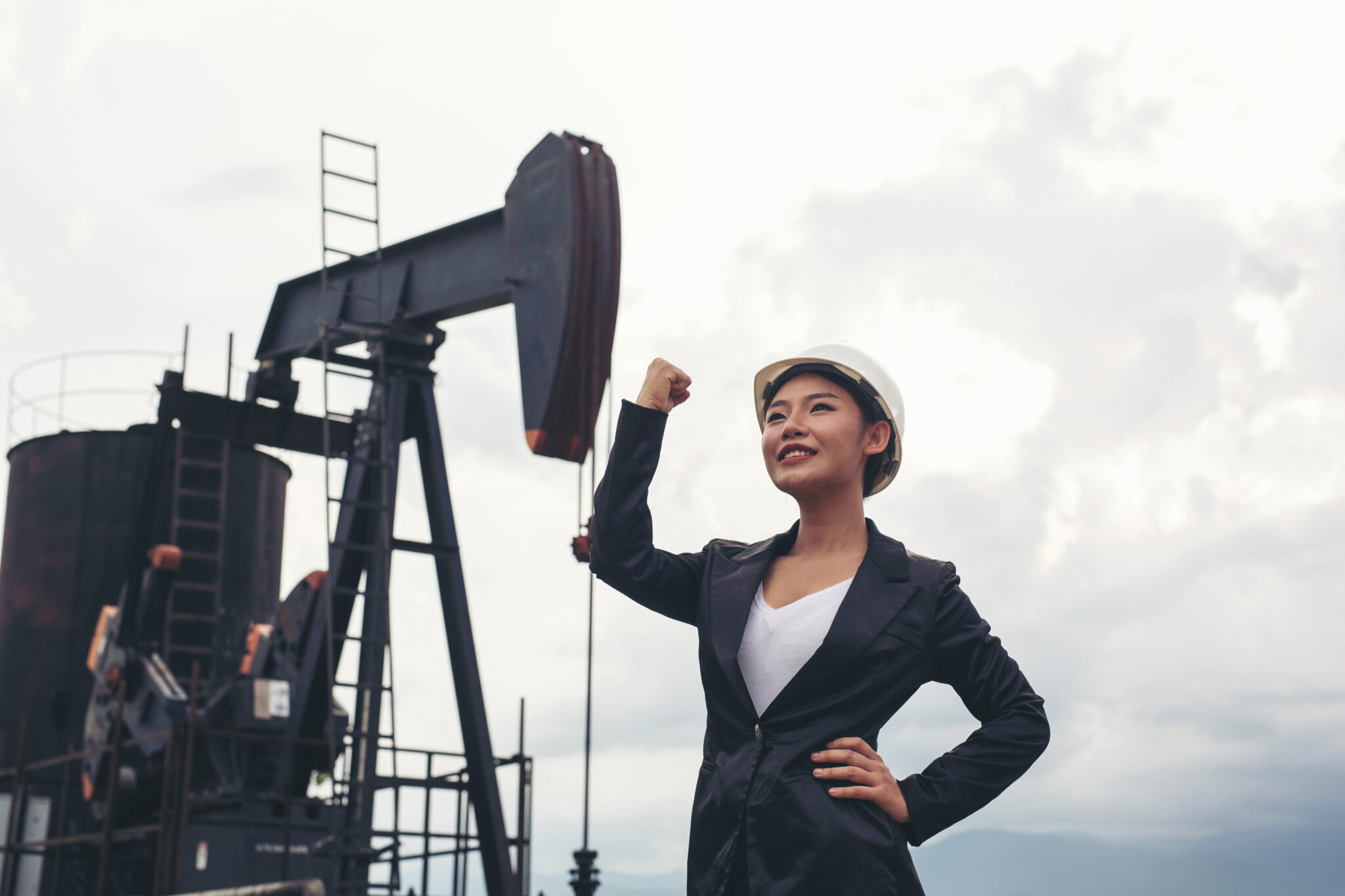 female engineer standing with working oil pumps with white sky